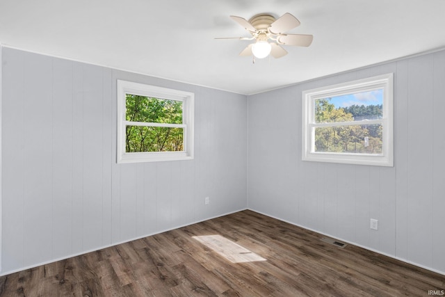 spare room with dark hardwood / wood-style flooring, a wealth of natural light, wooden walls, and ceiling fan