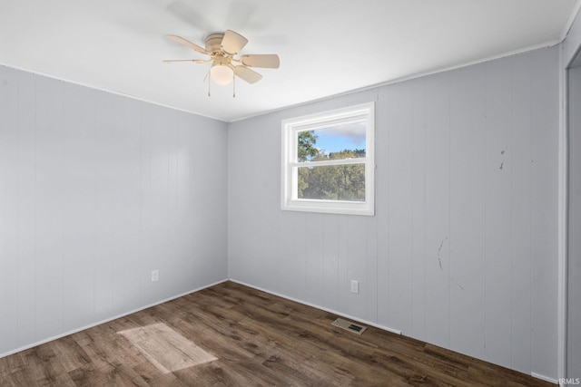 empty room with wooden walls, dark hardwood / wood-style flooring, and ceiling fan