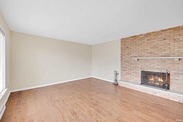 unfurnished living room with a fireplace, hardwood / wood-style floors, plenty of natural light, and a baseboard heating unit