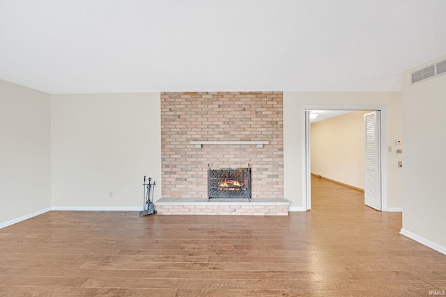 unfurnished living room with light wood-type flooring and a brick fireplace