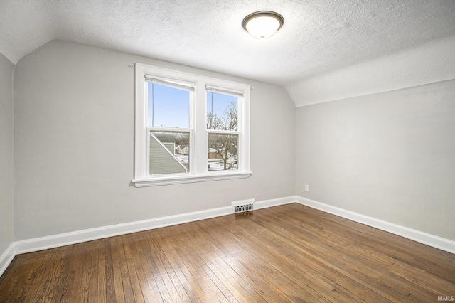 additional living space with hardwood / wood-style floors, a textured ceiling, and vaulted ceiling