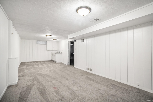 finished basement featuring a textured ceiling, visible vents, a sink, and light colored carpet