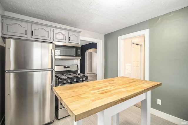 kitchen with arched walkways, gray cabinets, appliances with stainless steel finishes, wood counters, and a textured ceiling