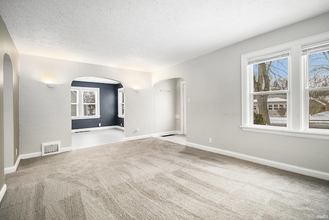 unfurnished room with arched walkways, a textured ceiling, visible vents, baseboards, and carpet