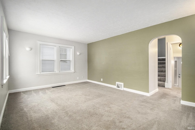 carpeted spare room with arched walkways, visible vents, a textured ceiling, and baseboards