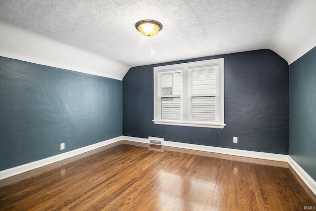 additional living space with a textured ceiling, vaulted ceiling, and hardwood / wood-style flooring