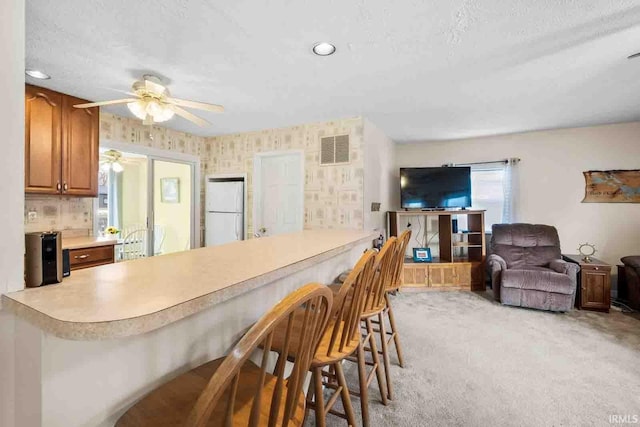 kitchen with a breakfast bar area, white fridge, ceiling fan, light carpet, and a textured ceiling