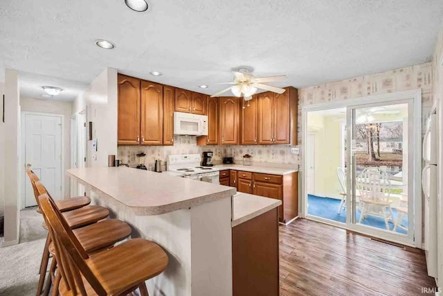 kitchen featuring a kitchen bar, white appliances, ceiling fan, kitchen peninsula, and a textured ceiling