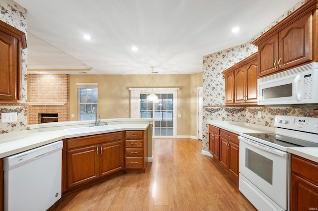 kitchen featuring sink, a brick fireplace, pendant lighting, white appliances, and light wood-type flooring