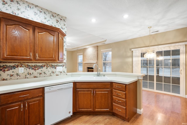 kitchen with kitchen peninsula, white dishwasher, sink, decorative light fixtures, and light hardwood / wood-style floors