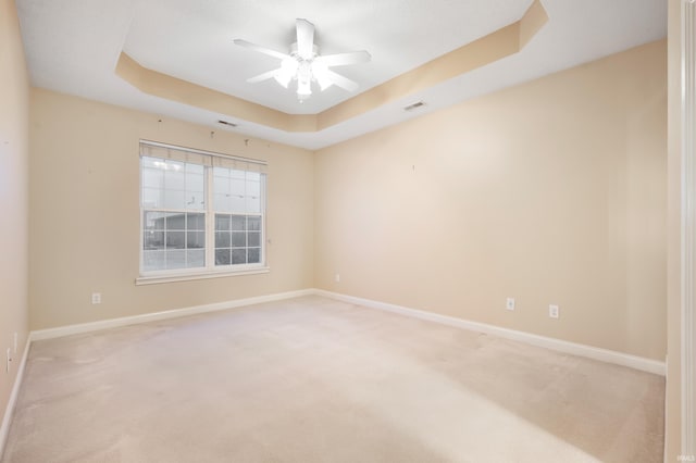 empty room with ceiling fan, light colored carpet, and a tray ceiling