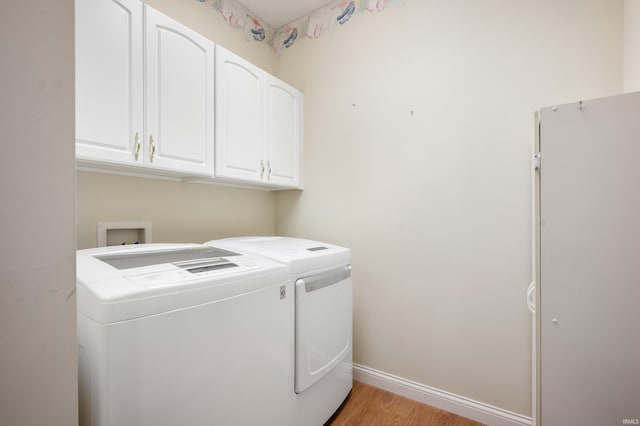 clothes washing area with washer and clothes dryer, cabinets, and light hardwood / wood-style flooring