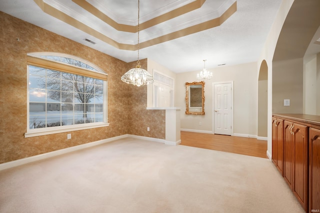 spare room featuring a raised ceiling, ornamental molding, light carpet, and a chandelier