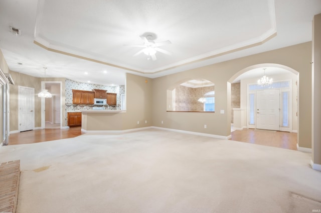 unfurnished living room featuring a raised ceiling, crown molding, ceiling fan, and light carpet