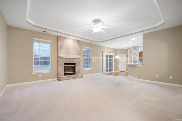 unfurnished living room with a tray ceiling, ceiling fan, a fireplace, and crown molding