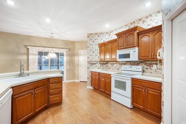 kitchen featuring sink, hanging light fixtures, a chandelier, white appliances, and light wood-type flooring