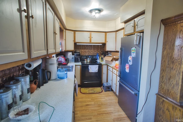 kitchen featuring black electric range oven, sink, refrigerator, light hardwood / wood-style floors, and backsplash