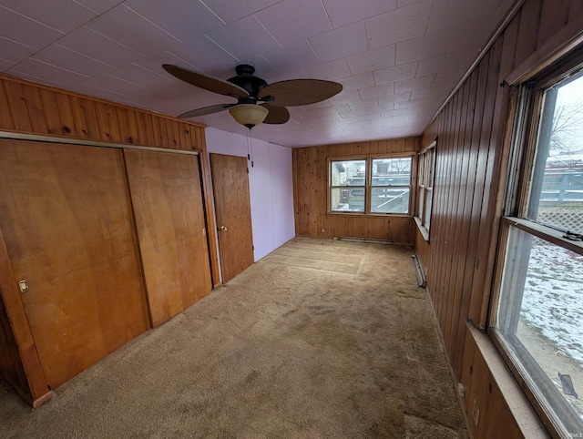 spare room featuring a wealth of natural light, wooden walls, ceiling fan, and light colored carpet