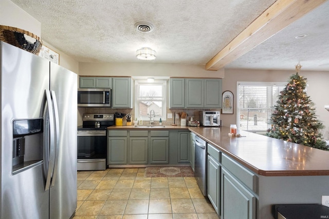 kitchen with sink, kitchen peninsula, decorative backsplash, light tile patterned floors, and appliances with stainless steel finishes