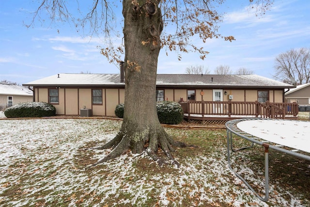 snow covered back of property featuring a wooden deck, cooling unit, and a trampoline