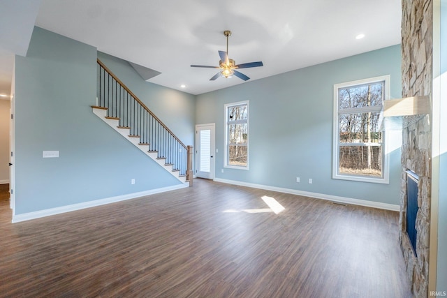 unfurnished living room featuring a stone fireplace, ceiling fan, and dark wood-type flooring