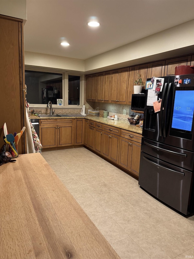 kitchen featuring decorative backsplash, black fridge, sink, and light stone countertops