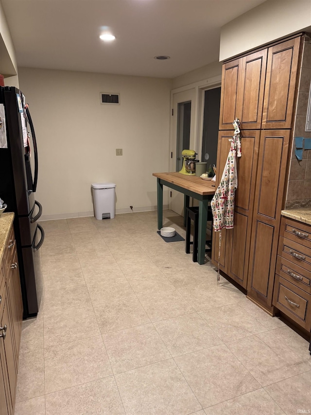 kitchen with black fridge, light tile patterned flooring, and light stone countertops