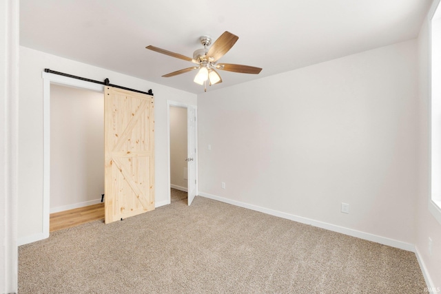 unfurnished bedroom featuring ceiling fan, a barn door, and light carpet