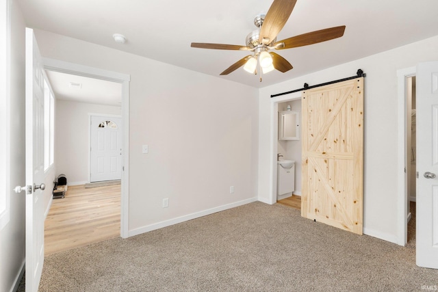 unfurnished bedroom with light carpet, a barn door, and ceiling fan