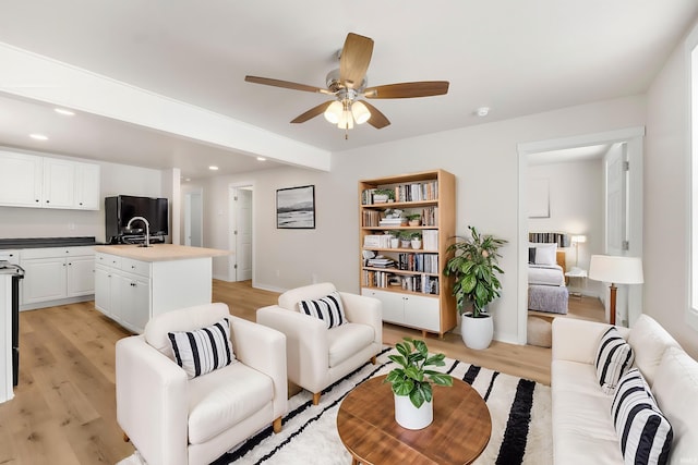 living room with ceiling fan, sink, and light wood-type flooring