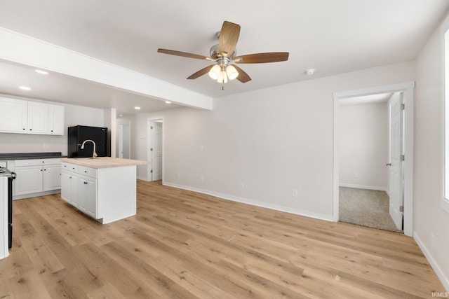 kitchen with white cabinetry, black refrigerator, light hardwood / wood-style floors, and a center island with sink