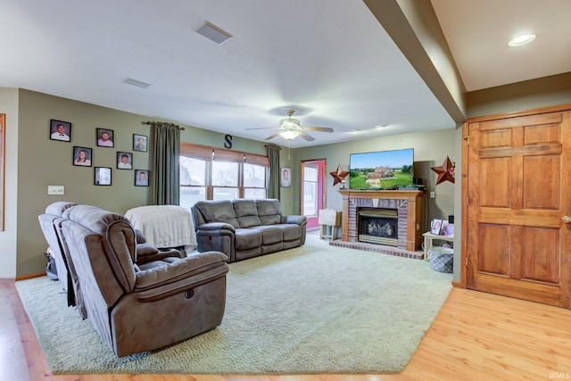 living room featuring ceiling fan, light wood-type flooring, and a brick fireplace