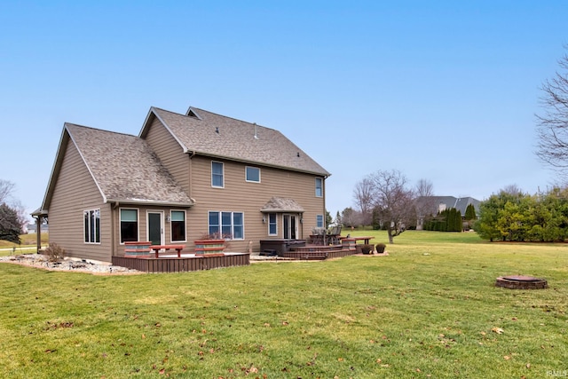 back of property with a lawn, a wooden deck, and an outdoor fire pit