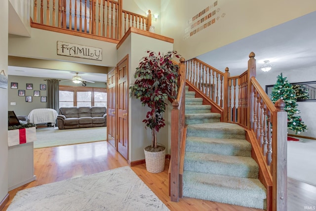 stairway with ceiling fan, a towering ceiling, and wood-type flooring