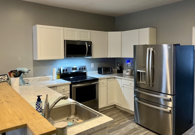 kitchen with hardwood / wood-style floors, sink, appliances with stainless steel finishes, butcher block countertops, and white cabinetry