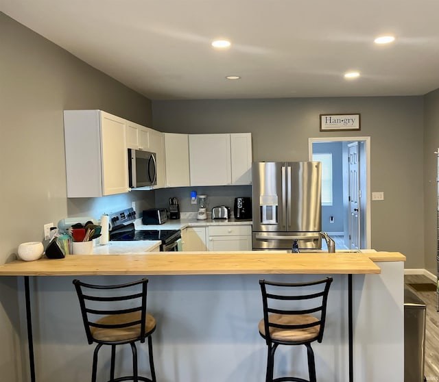 kitchen featuring kitchen peninsula, appliances with stainless steel finishes, a kitchen bar, and white cabinetry