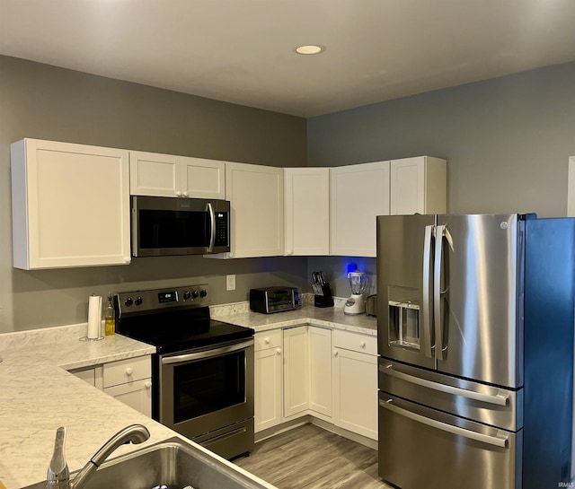 kitchen featuring white cabinetry, stainless steel appliances, light stone counters, and light hardwood / wood-style floors