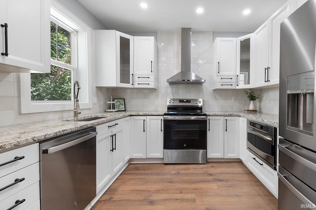 kitchen with white cabinets, sink, wall chimney exhaust hood, appliances with stainless steel finishes, and light stone counters