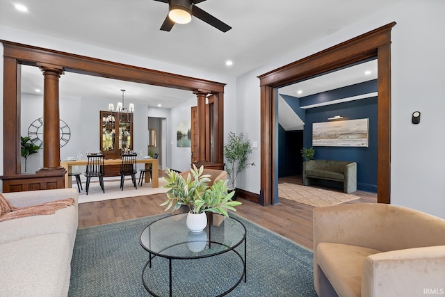 living room with ornate columns, light hardwood / wood-style floors, and ceiling fan with notable chandelier