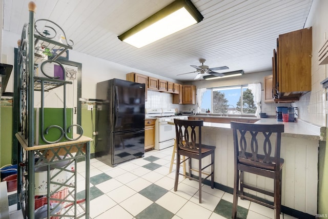 kitchen featuring black refrigerator, backsplash, white range oven, and kitchen peninsula