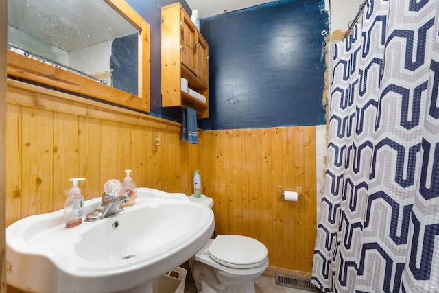 bathroom with curtained shower, wood walls, sink, and toilet