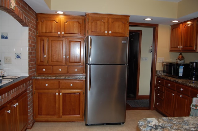 kitchen featuring stainless steel fridge, dark stone countertops, and backsplash