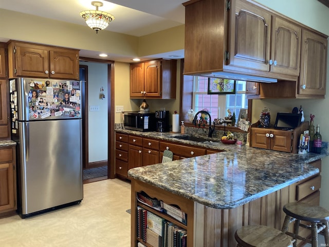 kitchen featuring kitchen peninsula, stainless steel appliances, dark stone countertops, and sink