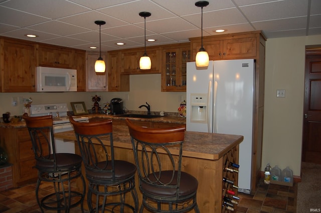 kitchen featuring a kitchen bar, a drop ceiling, white appliances, sink, and pendant lighting