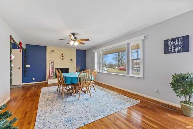 dining area featuring a fireplace, hardwood / wood-style flooring, and ceiling fan