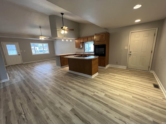 kitchen featuring gas cooktop, a kitchen island with sink, ceiling fan, wood-type flooring, and oven