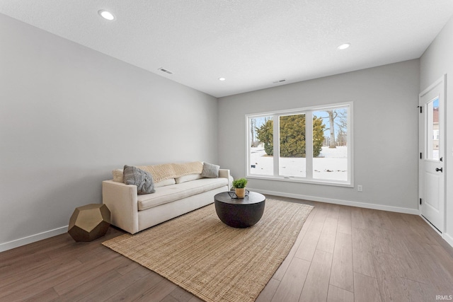 living area with recessed lighting, a textured ceiling, baseboards, and wood finished floors