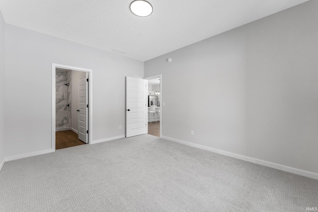 unfurnished bedroom with a textured ceiling, carpet, ensuite bathroom, and baseboards