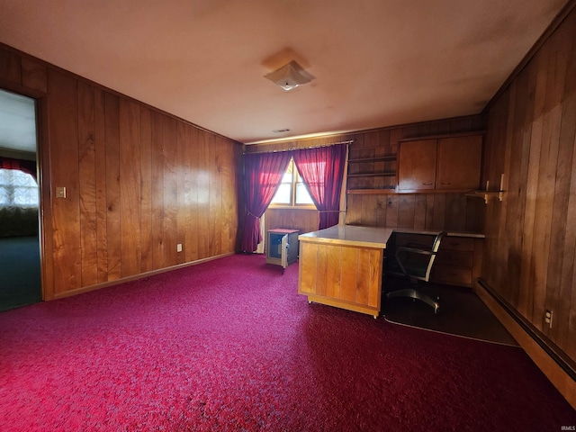 unfurnished office featuring dark colored carpet, built in desk, wooden walls, and a baseboard heating unit