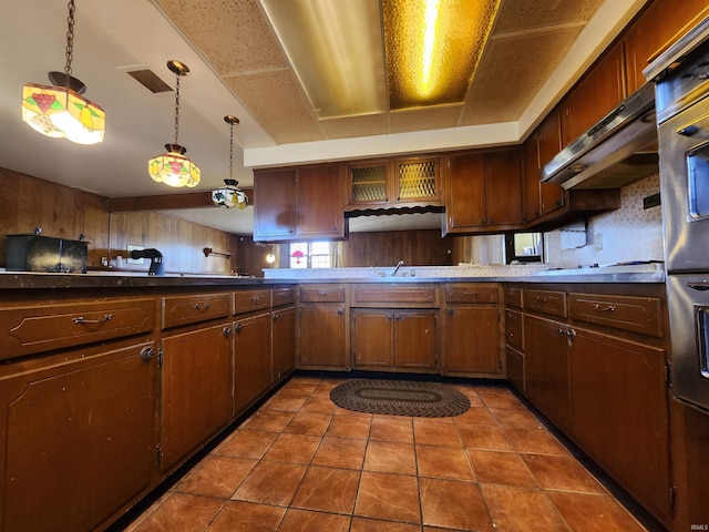 kitchen with dark tile patterned floors, sink, kitchen peninsula, and hanging light fixtures